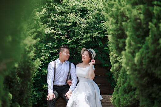 Asian couple sitting on a bench surrounded by lush greenery, capturing a romantic moment.